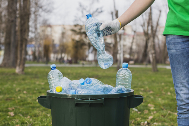 zdjęcie przedstawia osobę wyrzucającą plastikowe butelki do kosza - recycling, harmonogram odbioru odpadów komunalnych